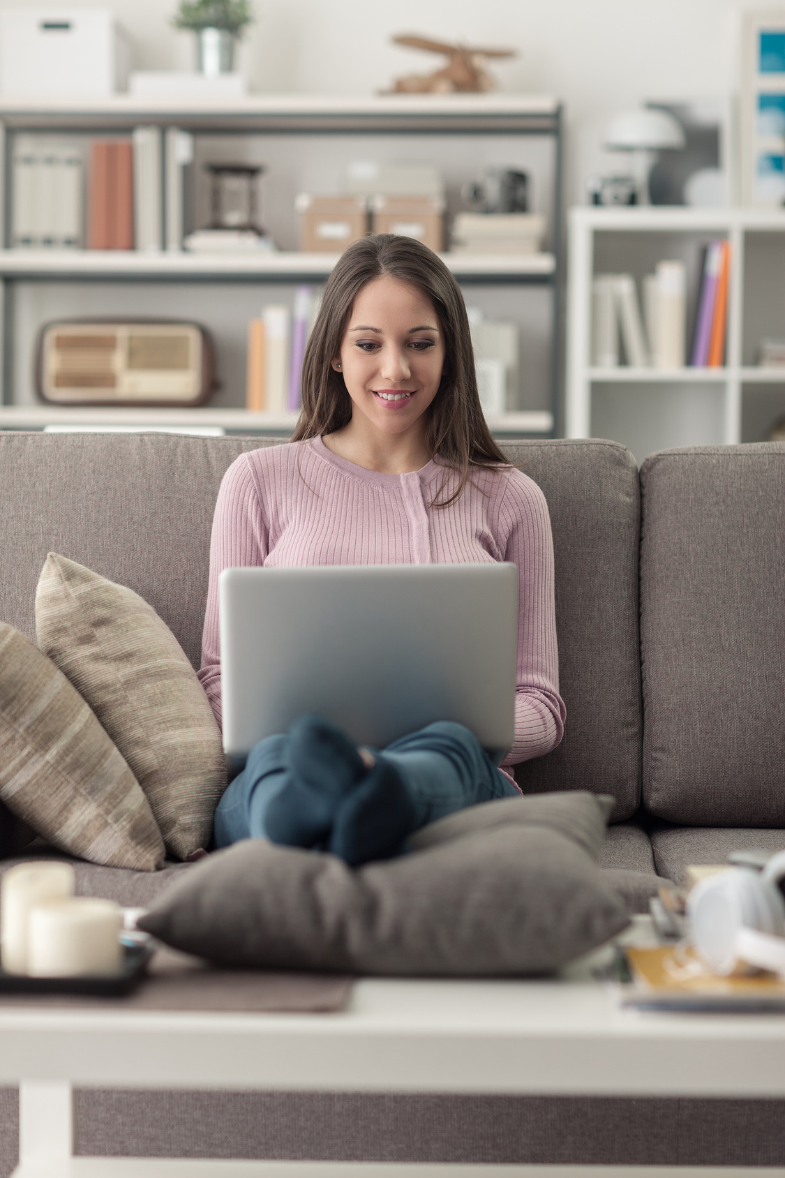 Young woman relaxing at home, she is sitting on the couch in the living room, using a laptop and social networking