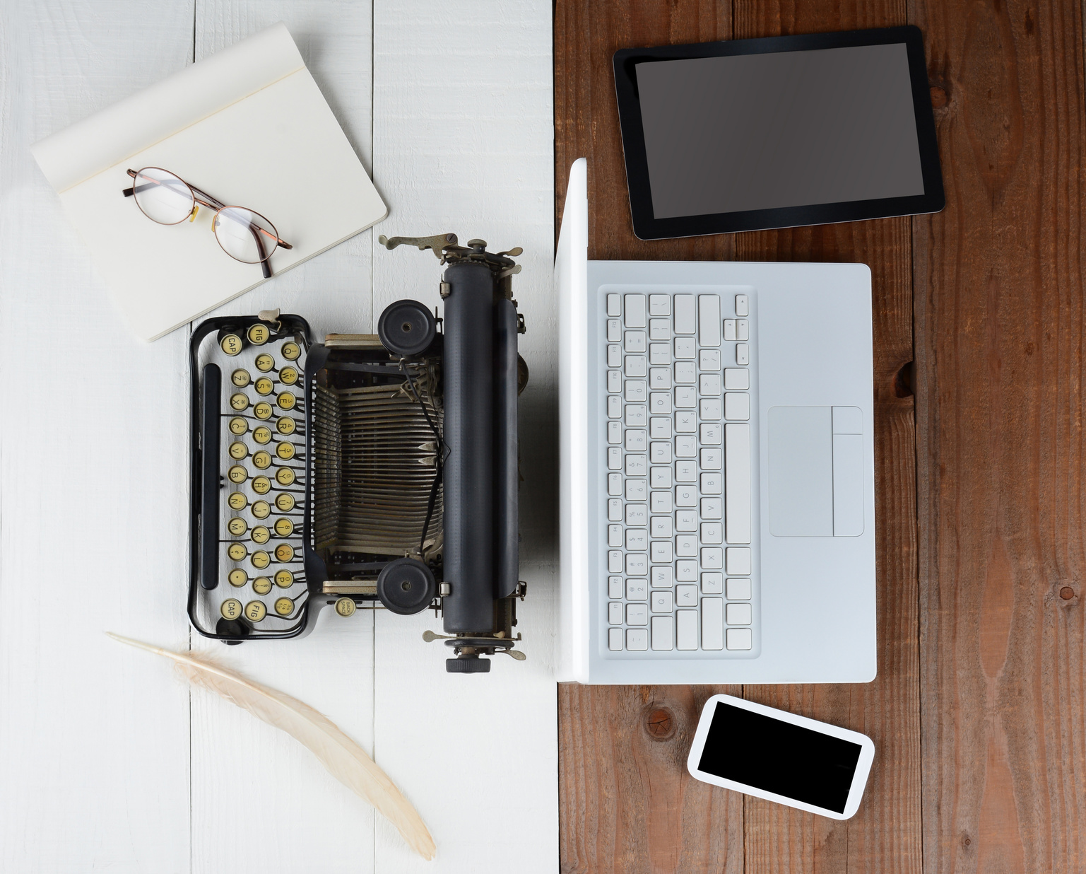 Overhead shot of and old fashioned desk with typewriter and quill pen back-to-back with a modern set up with laptop computer, tablet and cell phone, (Phone and Tablet created in Photoshop - not real)