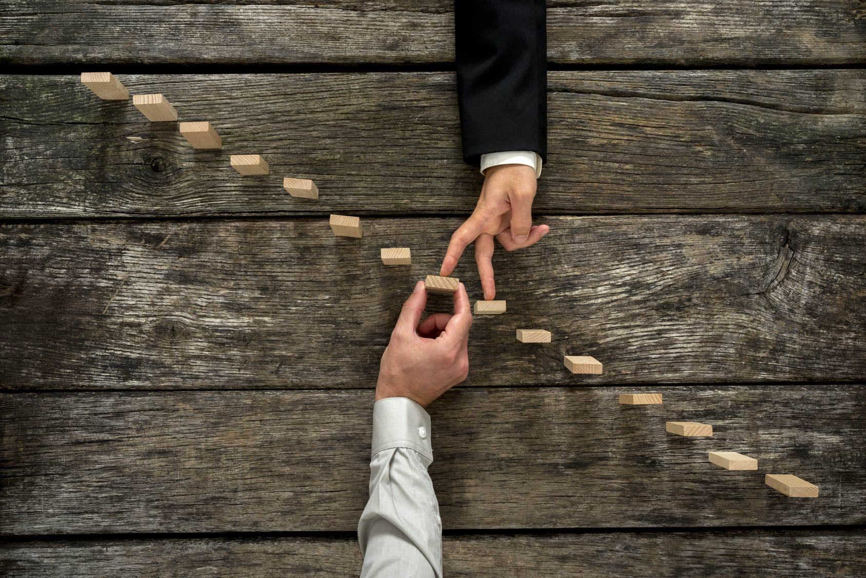 Conceptual image of business partnership and support - businessman supporting wooden step in a staircase made of pegs as his partner walks his fingers up towards growth, achievement and development.
